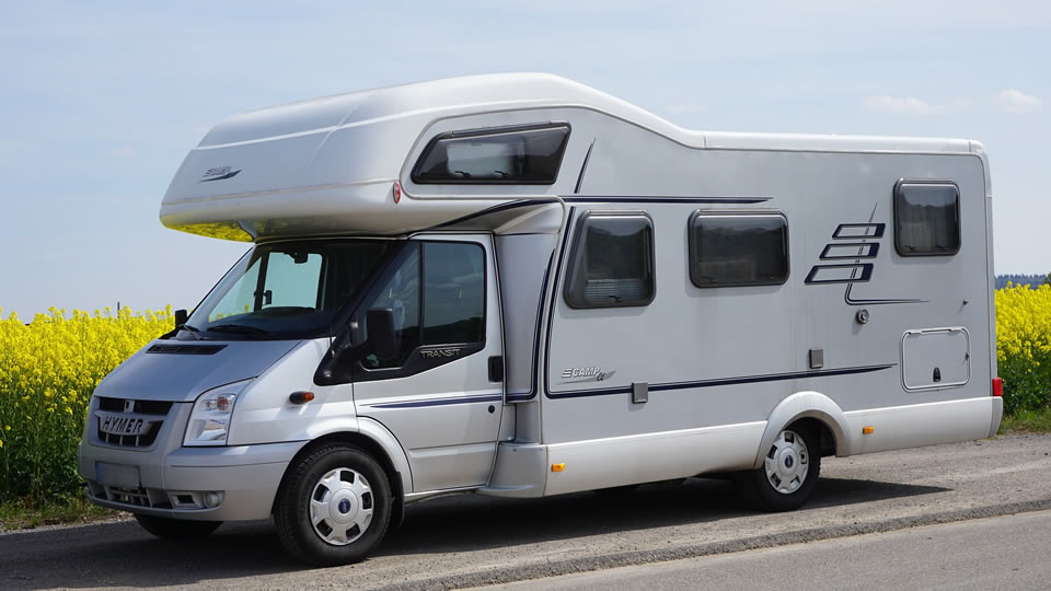 Un camping-car est garé au bord d’une route par temps clair, avec un champ de fleurs jaunes en arrière-plan.
